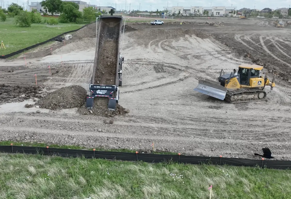 Aerial view of a dump truck delivering fill dirt to an active Texas job site
